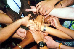 Arms outstretched towards the center of a group of people with their hands clasping one-another